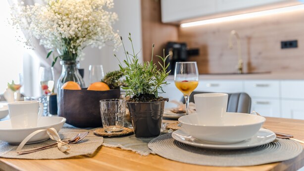 Una mesa de comedor dispuesta con platos blancos, tazas y una planta en maceta.