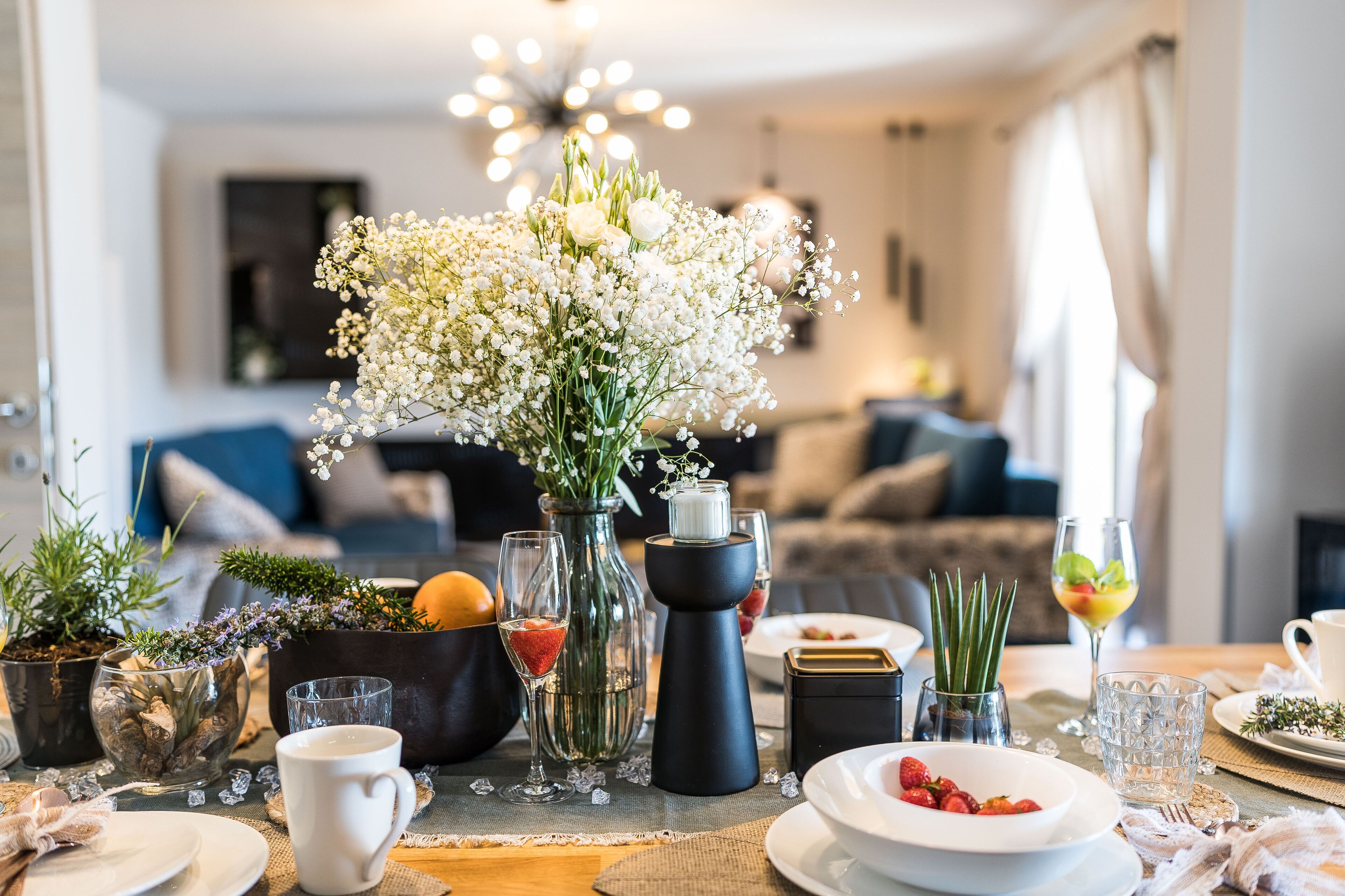 A dining table set with various dishes, a vase of flowers, and a modern chandelier in the background.