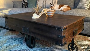 Un salon comprenant un canapé, une table basse en bois sur roulettes et un tapis à motifs.