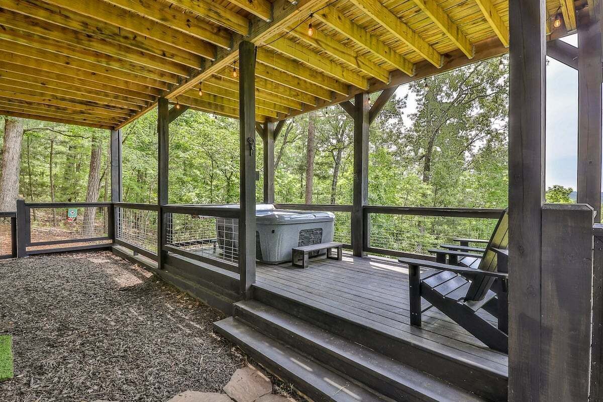 A covered outdoor deck with a hot tub, seating area, and steps leading to a grassy area.