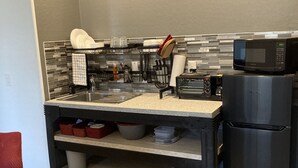 Eine kompakte Küche mit Mikrowelle, Kühlschrank und einer Arbeitsplatte mit verschiedenen Küchenutensilien.