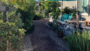 Ein Gartenweg führt zu einer Terrasse mit einem blauen Sonnenschirm, umgeben von Pflanzen und einer Steinmauer.
