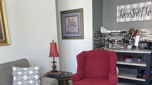 Ein Wohnzimmer mit grauem Sofa, einem roten Sessel, einem schwarzen Couchtisch und einer Küchenzeile mit gefliestem Rücksprung und verschiedenen Küchengegenständen.