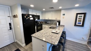 Una cocina moderna con armarios blancos, un refrigerador negro, encimeras de granito y una estufa empotrada.