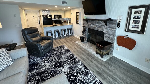 Una sala de estar moderna con un sillón de cuero negro, un tapete estampado, una chimenea y un televisor montado en la pared.