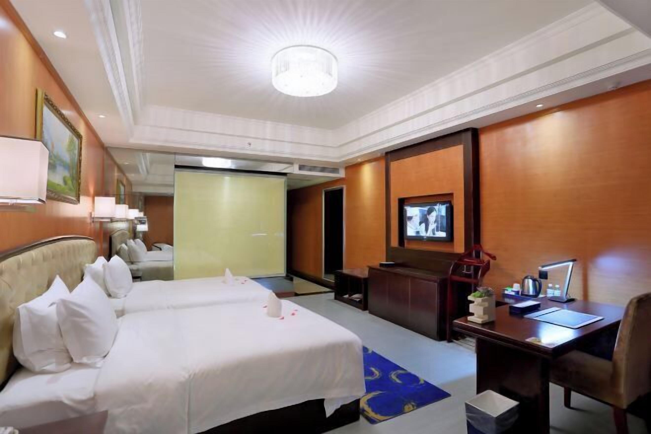 A hotel room with two beds, a desk, a chair, a television, and a lamp.