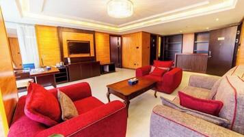 A hotel room with a large flat-screen TV, a wooden accent wall, a red sofa, a grey sofa, and a wooden coffee table.