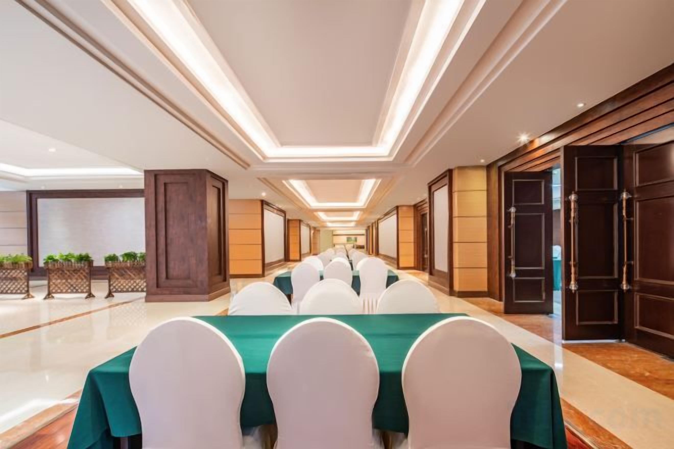 A conference room with a long table, white chairs, and a green tablecloth.