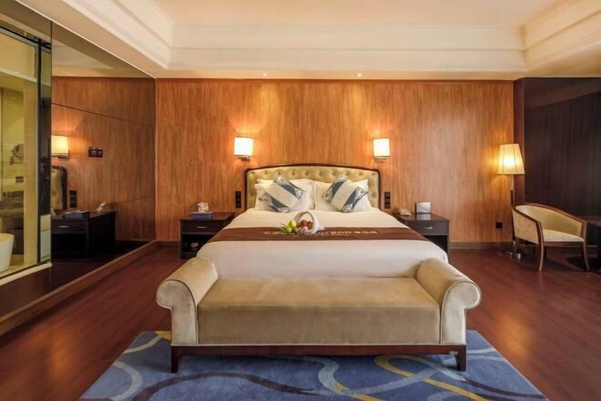 A hotel room with a large bed, wooden paneling, two bedside lamps, a nightstand, and a chair.