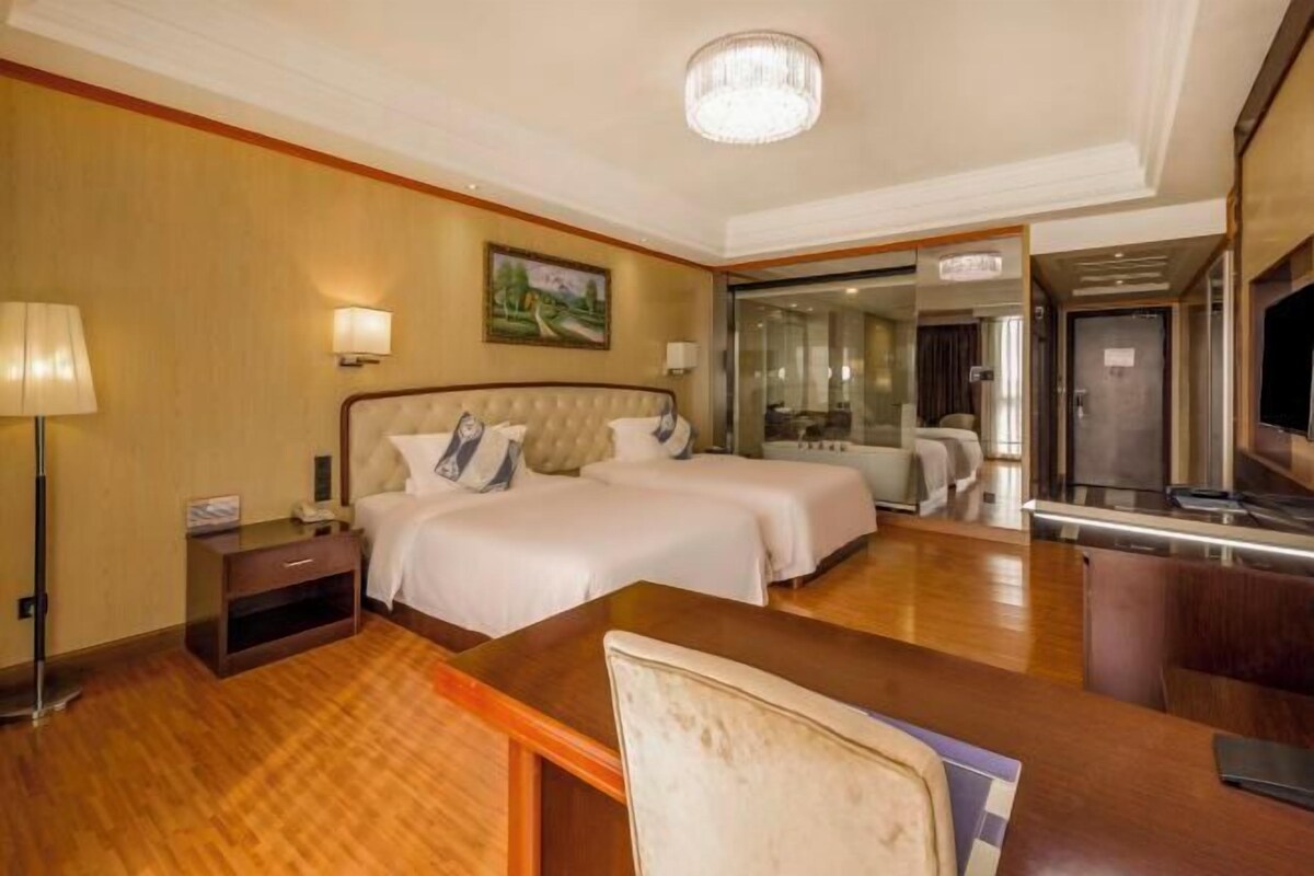 A hotel room with a large bed, a desk, a chair, a TV, and a painting on the wall.