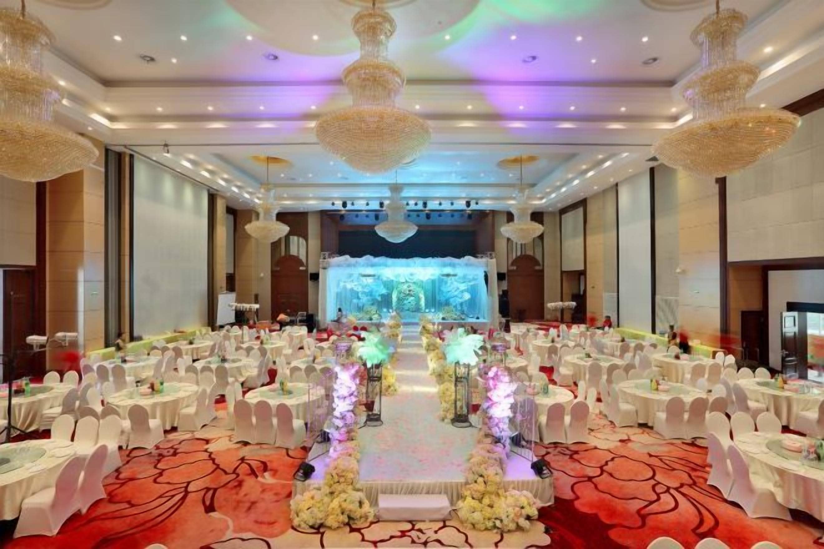 A banquet hall with round tables, a stage, and a red carpet.