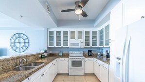 Eine moderne Küche mit weißen Schränken, Granit Arbeitsplatten, einem Backofen und einem Deckenventilator.