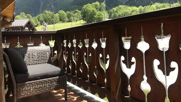 Un balcon avec un fauteuil en osier et une balustrade en bois ornée de motifs décoratifs.