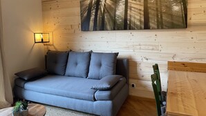Un salon moderne avec un canapé gris, un tableau représentant des arbres accroché au mur, une lampe sur pied et une petite plante en pot.