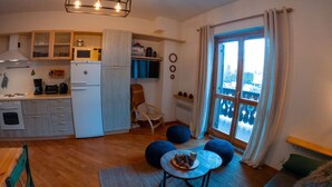 Une cuisine compacte dotée d’appareils électroménagers modernes, un coin repas avec une table et des chaises, et une grande fenêtre offrant une vue sur l’extérieur.