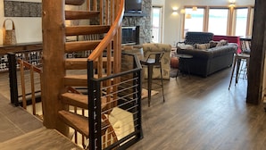 Un vaste espace de vie agrémenté d’un escalier en colimaçon en bois, d’une cheminée en pierre, d’une grande fenêtre offrant une vue imprenable et d’un coin salon confortable avec un canapé et des fauteuils.