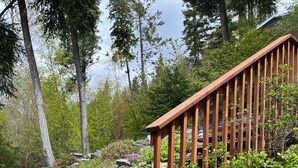 Une terrasse en bois dotée d’une rambarde, entourée d’une végétation luxuriante et de plantes en fleurs.