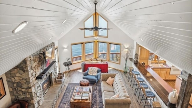 Un loft spacieux doté d’une cheminée en pierre, d’un grand canapé, d’un coin repas avec des tabourets de bar et offrant une vue sur l’océan grâce à de grandes fenêtres.