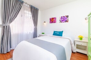 Ein Hotelzimmer mit einem Bett, einem Nachttisch, einer Lampe und zwei an der Wand befestigten Blumenbildern.