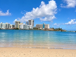 A coastal cityscape with a beach in the foreground and high-rise buildings in the background.