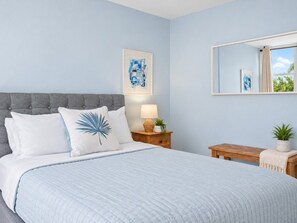 A bedroom with a bed, a nightstand, a mirror, and a window.
