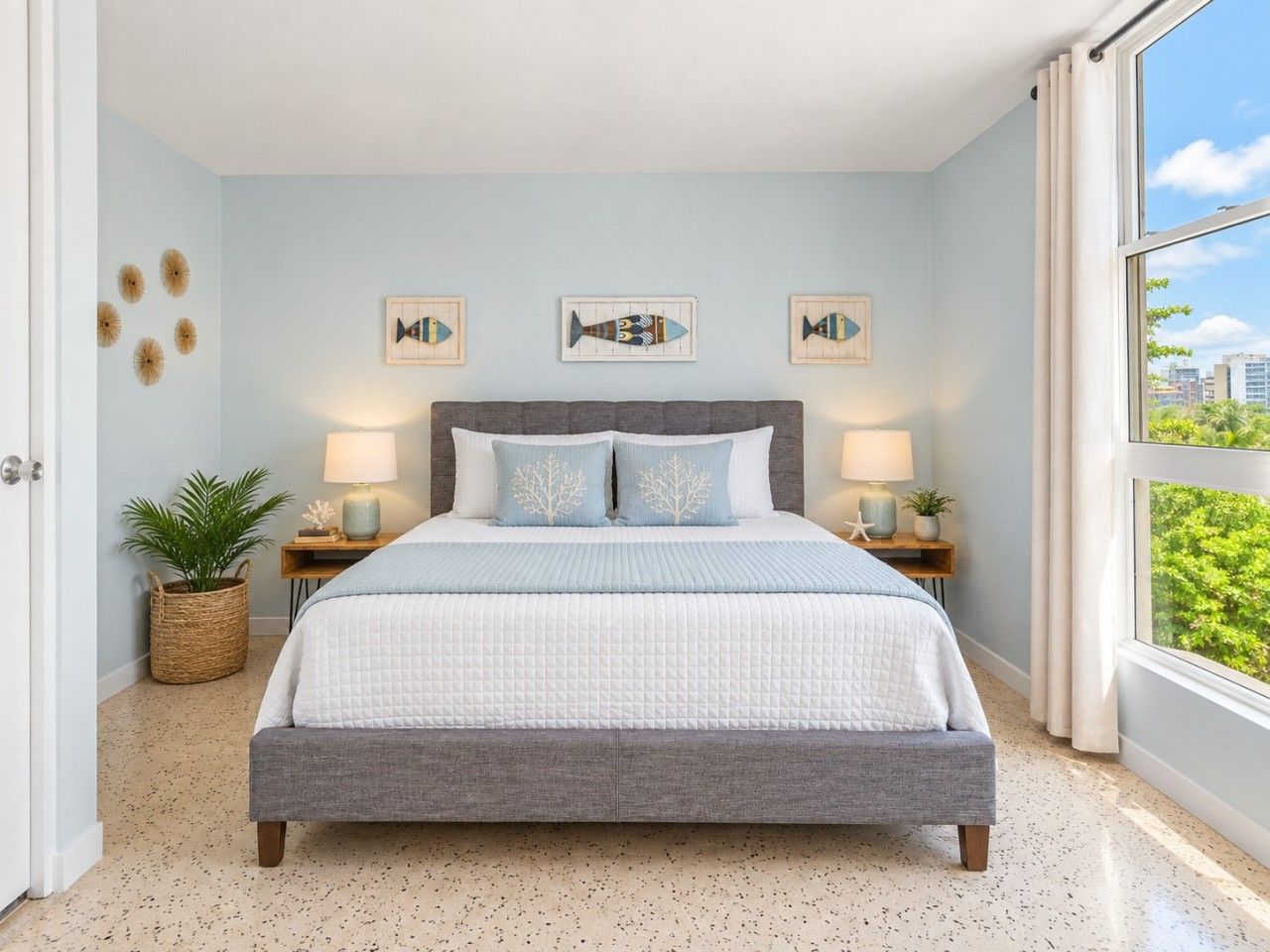 A bedroom with a bed, two bedside tables, wall art, and a view through a window.