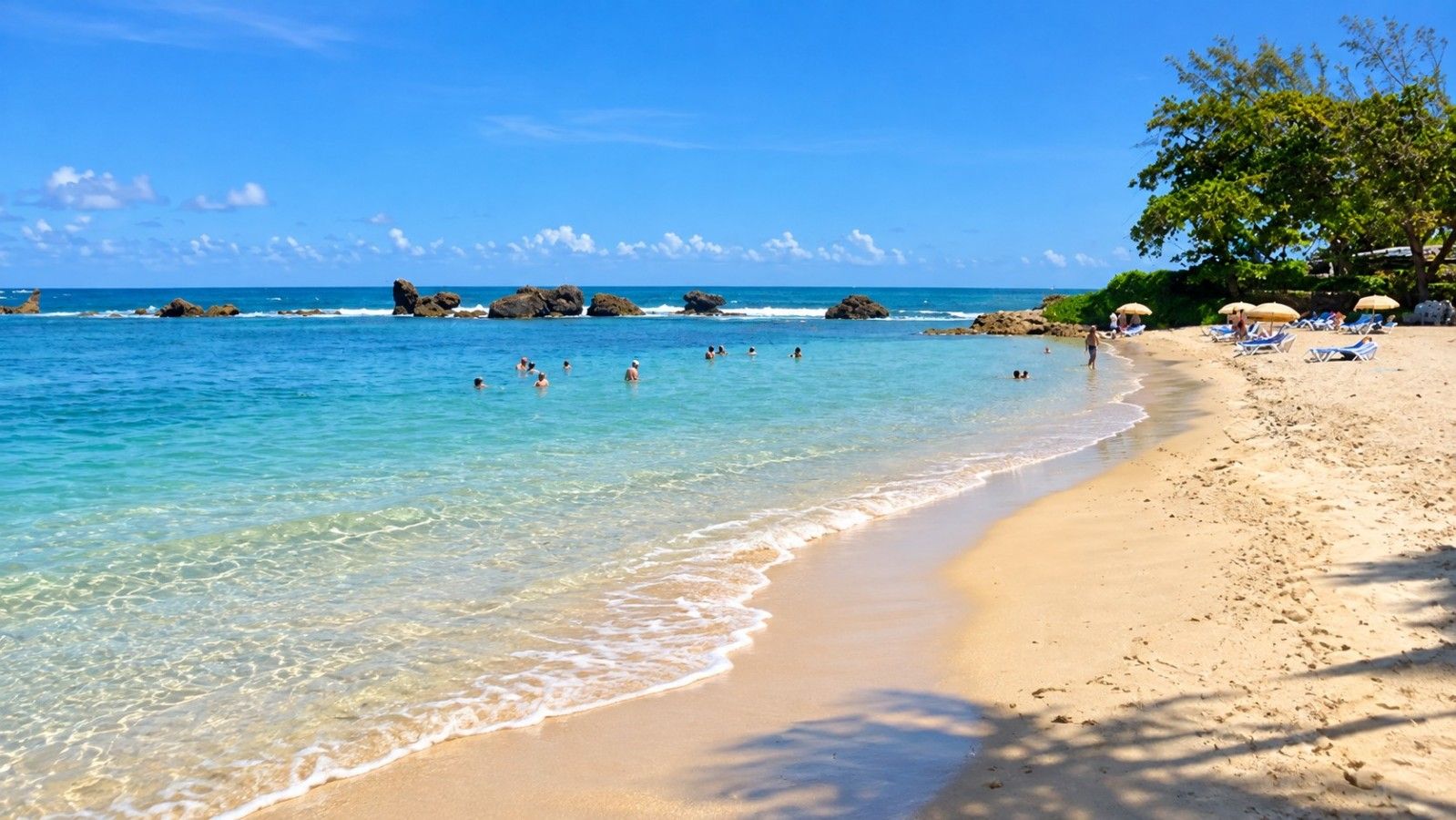 Une plage à l’eau claire, où l’on peut se baigner, avec des transats placés sous des parasols.
