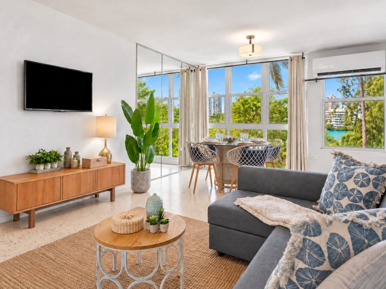 A modern living room with a sofa, a TV, a dining area with chairs, and large windows.