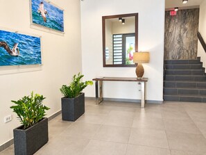 Um hall de entrada com balcão de recepção, espelho, plantas em vasos e escada.