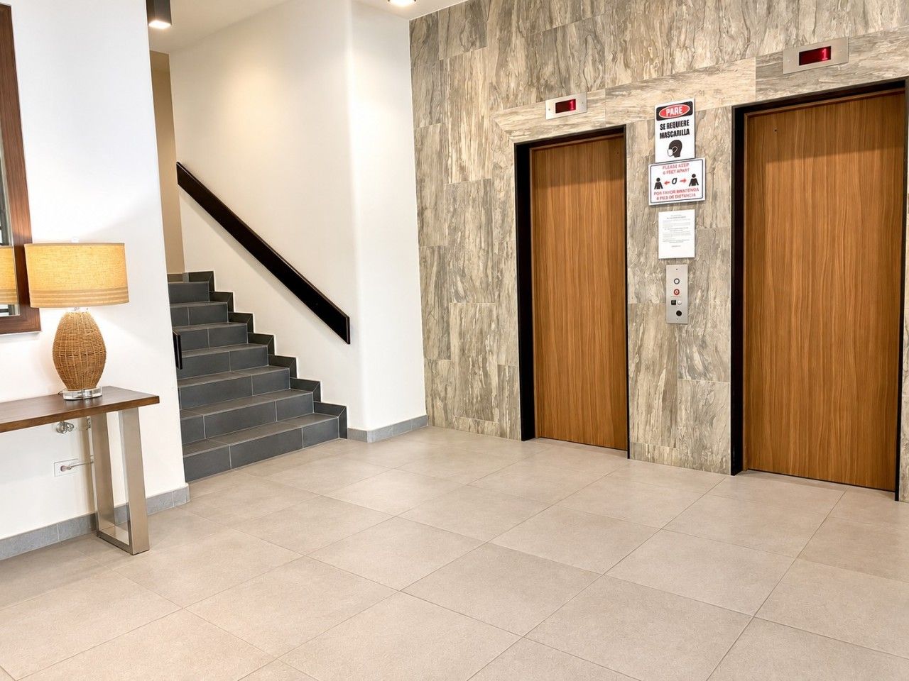 A modern interior with a staircase, a console table with a lamp, and two wooden doors with signs.