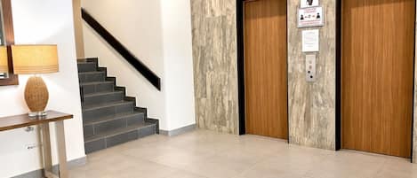 A modern interior with a staircase, a console table with a lamp, and two wooden doors with signs.