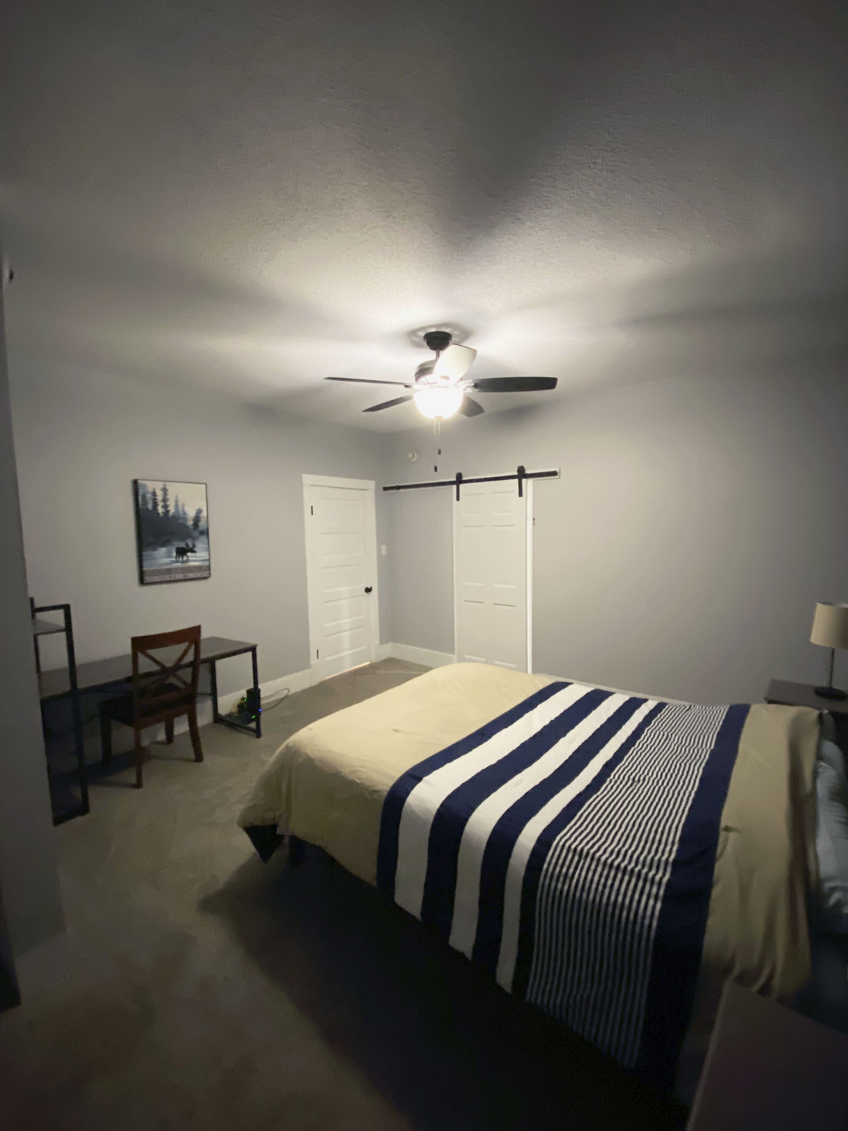 Un dormitorio con cama, escritorio, silla, ventilador de techo y puerta.