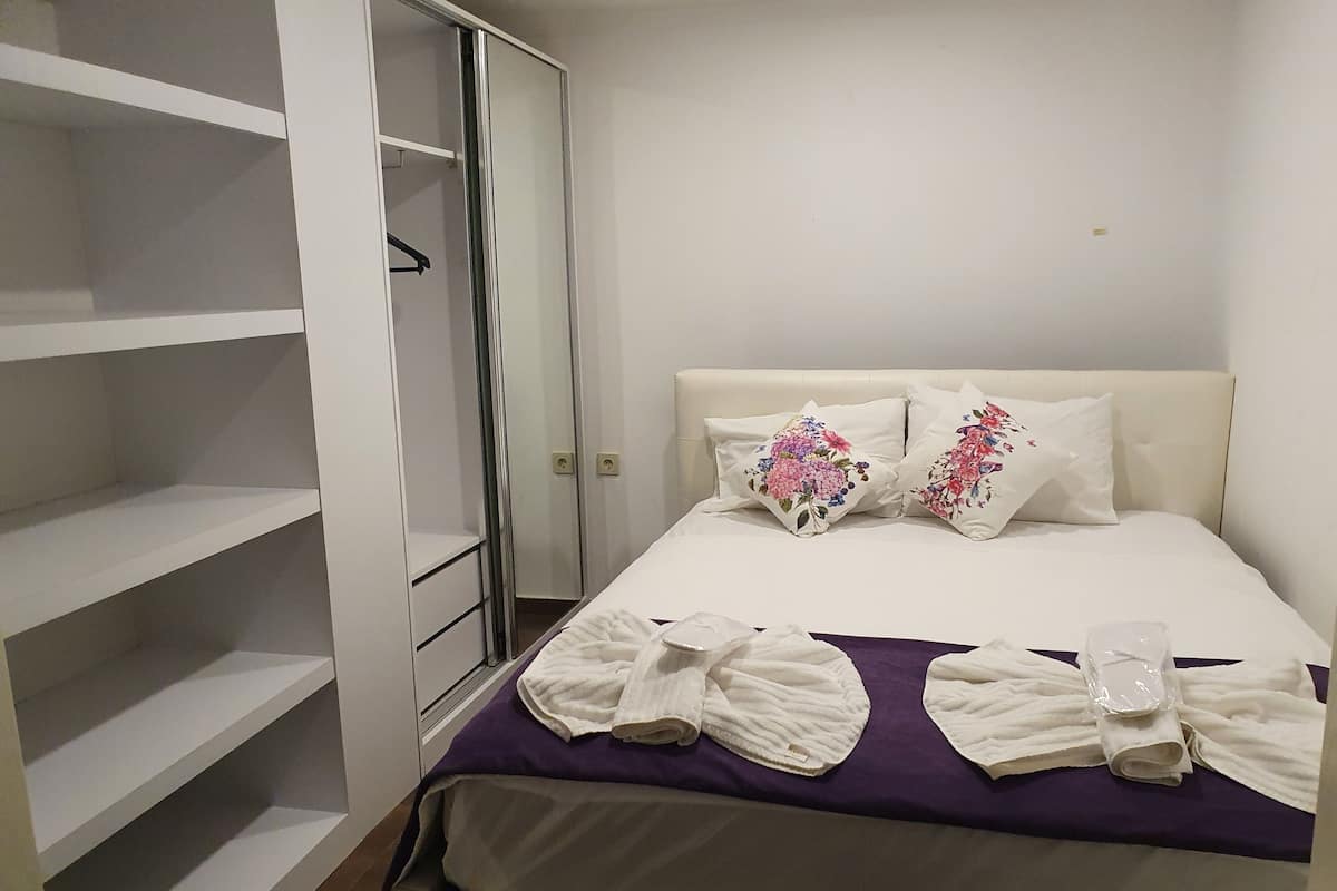 A neatly made bed with floral pillows, a purple blanket, and rolled towels.