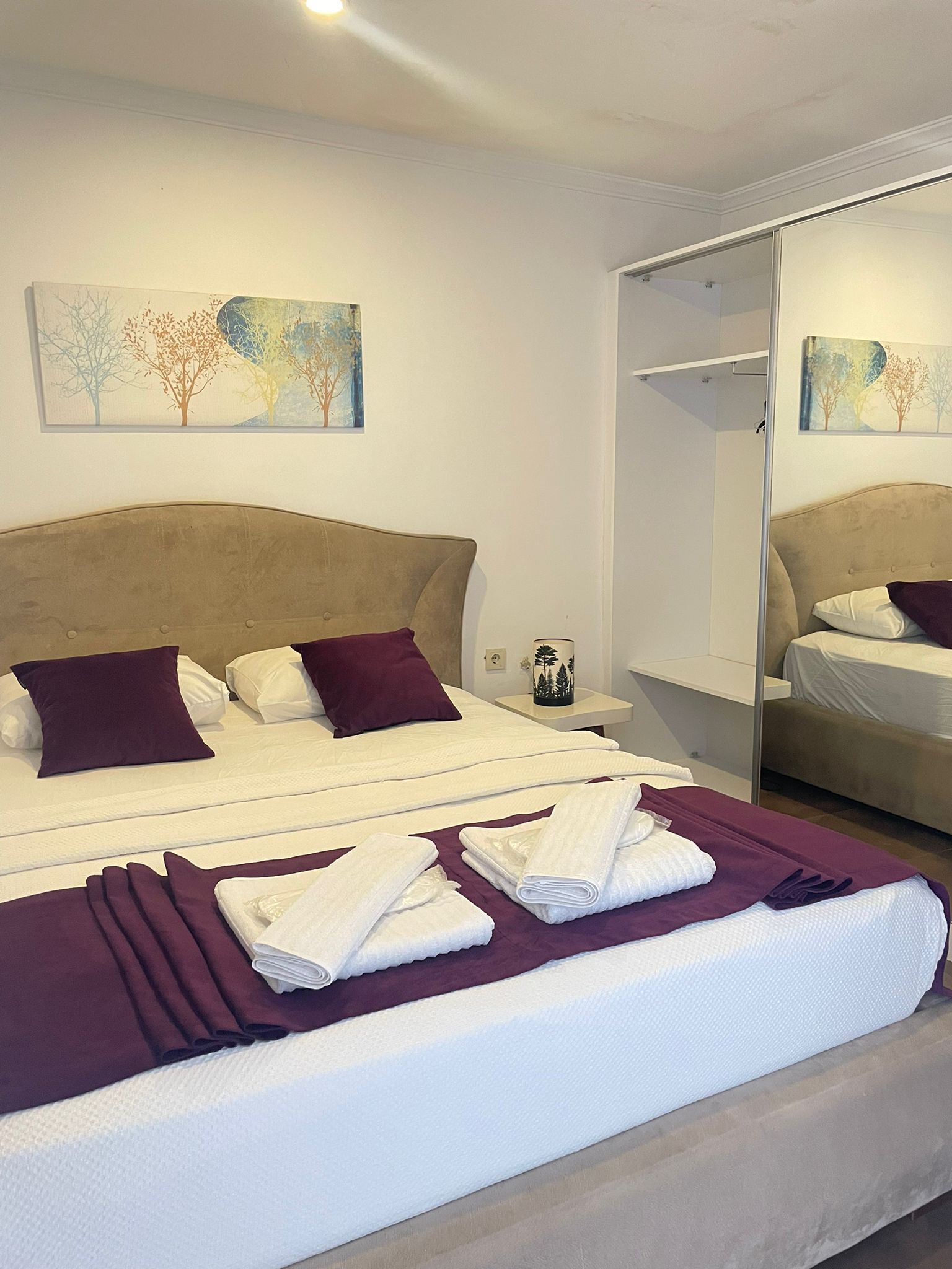 Une chambre d’hôtel avec un grand lit, une table de chevet, une commode, un miroir et deux tableaux accrochés au mur.