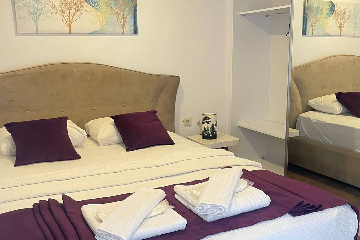 A hotel room with a large bed, a bedside table, a nightstand, a mirror, and two wall-mounted paintings.