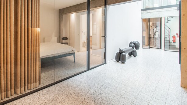 A modern bedroom with a bed, a glass partition, and a unique sculpture.