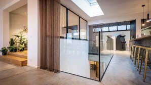 A modern interior with a glass partition, a kitchen area with bar stools, and a staircase leading to another level.
