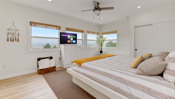 A bedroom with a bed, a TV, a ceiling fan, and a view of the city. - Cozy 3BR Renovated Home with Scenic Views! Near Downtown/Airport/Gaslamp Quarter (San Diego)