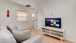 A modern living room with a flat-screen TV, white walls, and a grey sofa. - Cozy 3BR Renovated Home with Scenic Views! Near Downtown/Airport/Gaslamp Quarter (San Diego)