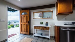 A kitchen with a wooden door, a window with blinds, a white console table, and a stainless steel dishwasher. - Cozy 3BR Renovated Home with Scenic Views! Near Downtown/Airport/Gaslamp Quarter (San Diego)