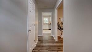 A hallway with wooden flooring, white walls, and a door leading to a kitchen area.