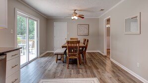 A dining area with a wooden table and chairs, a ceiling fan, and a view of the outdoors through a sliding glass door.