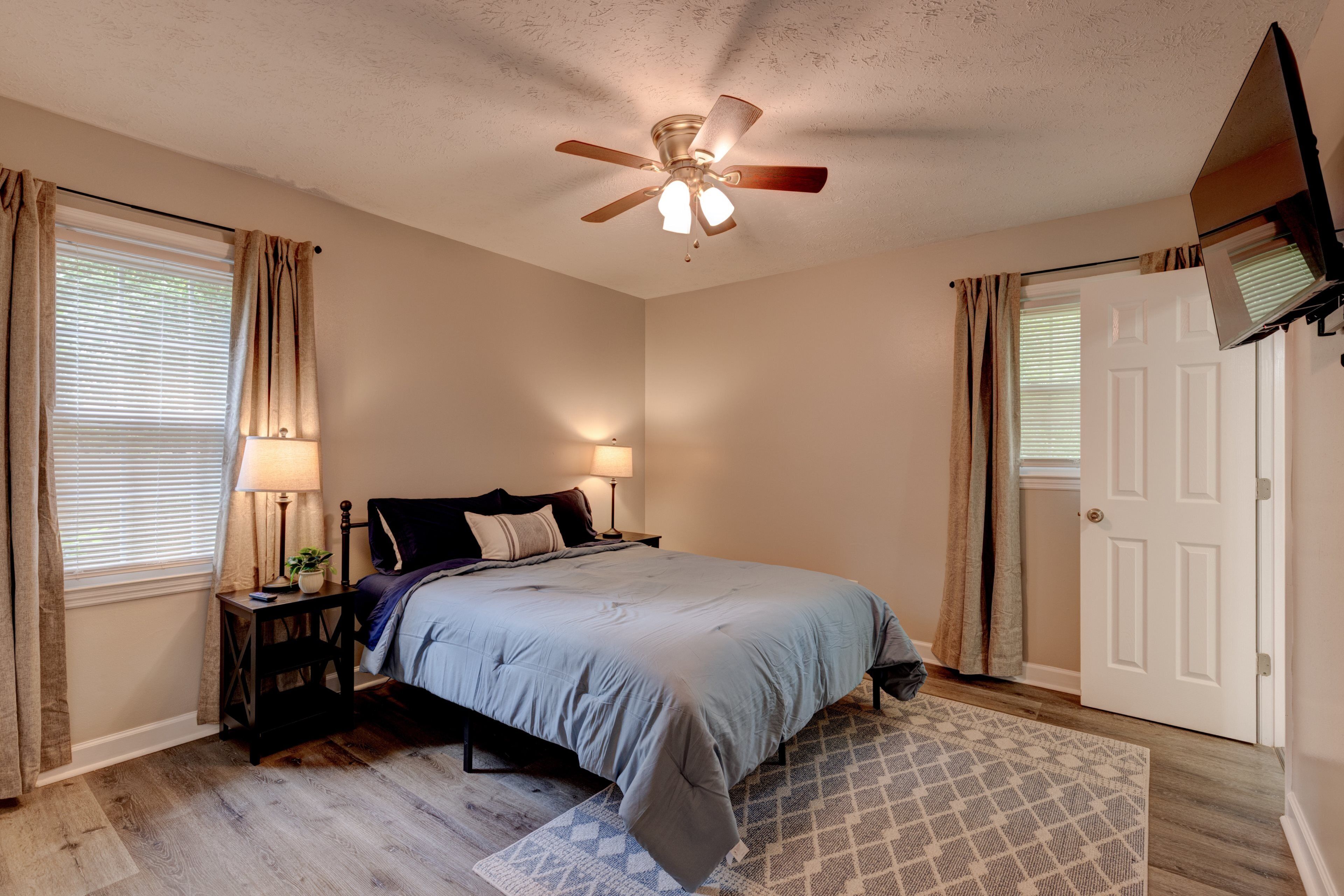 A bedroom with a bed, nightstands, a ceiling fan, a door, and a window with curtains.