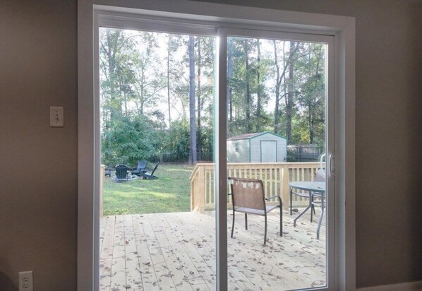A sliding glass door leading to a deck with a wooden floor and a view of a backyard with a lawn, a grill, and a shed.