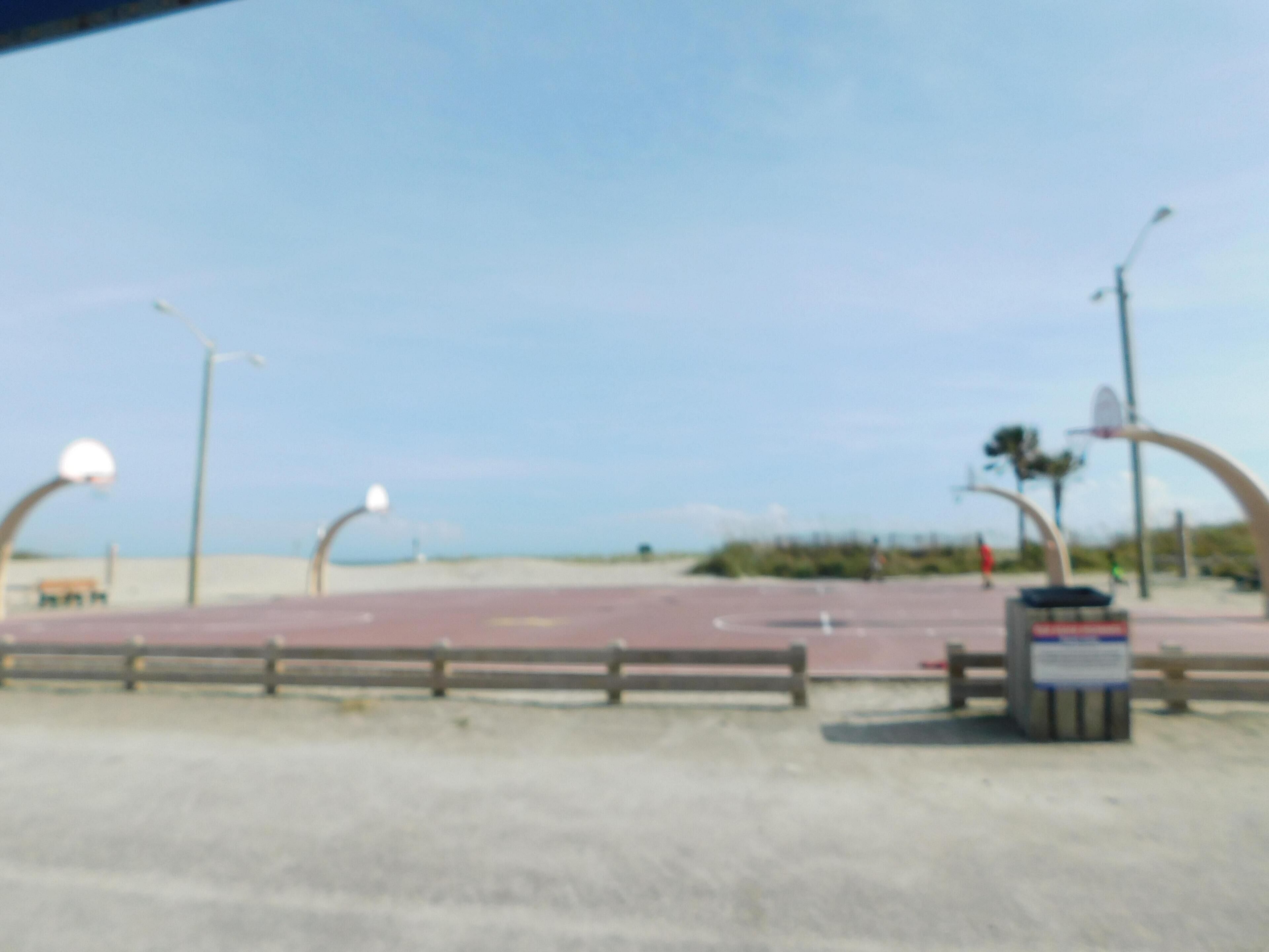A paved area with a fence, street lamps, and a trash bin.