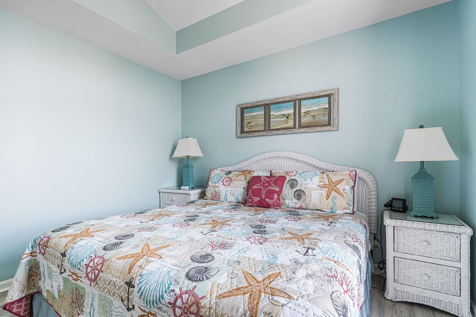 A bedroom with a bed, two nightstands, a wall-mounted picture, and a light blue wall.