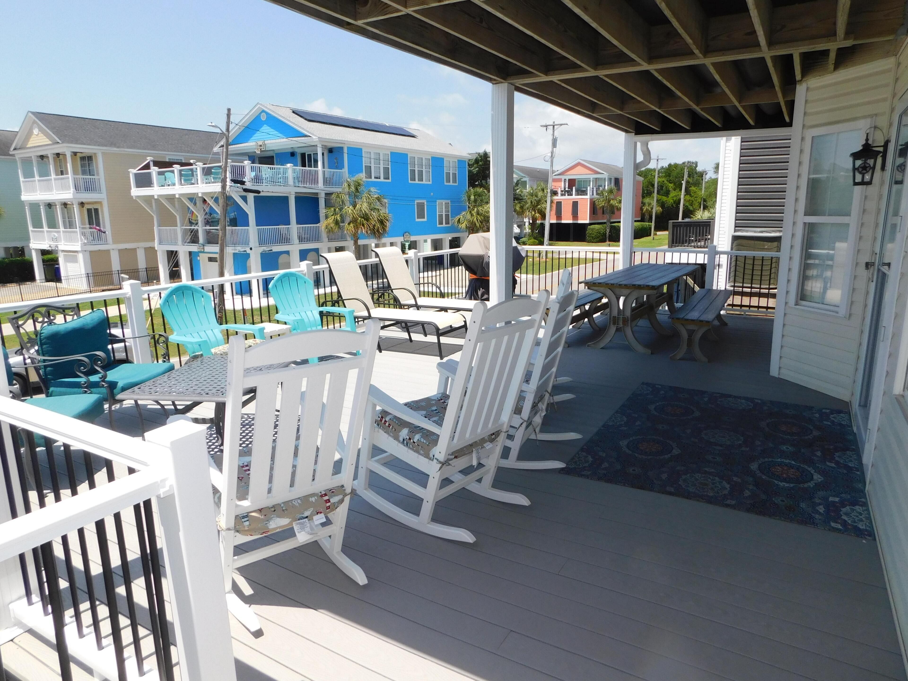 A covered outdoor area with white rocking chairs, a table, and a blue patterned rug.
