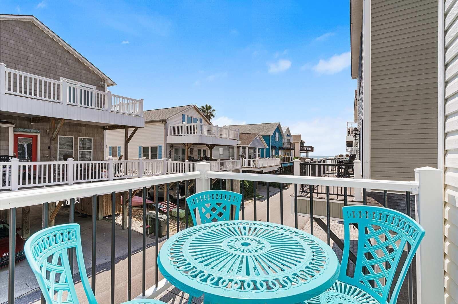Un balcon avec des chaises turquoise, une balustrade blanche et une vue sur les maisons voisines.