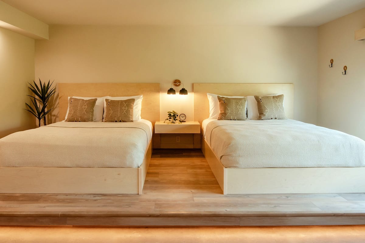 A double bed room with two nightstands, a small table, and a potted plant.
