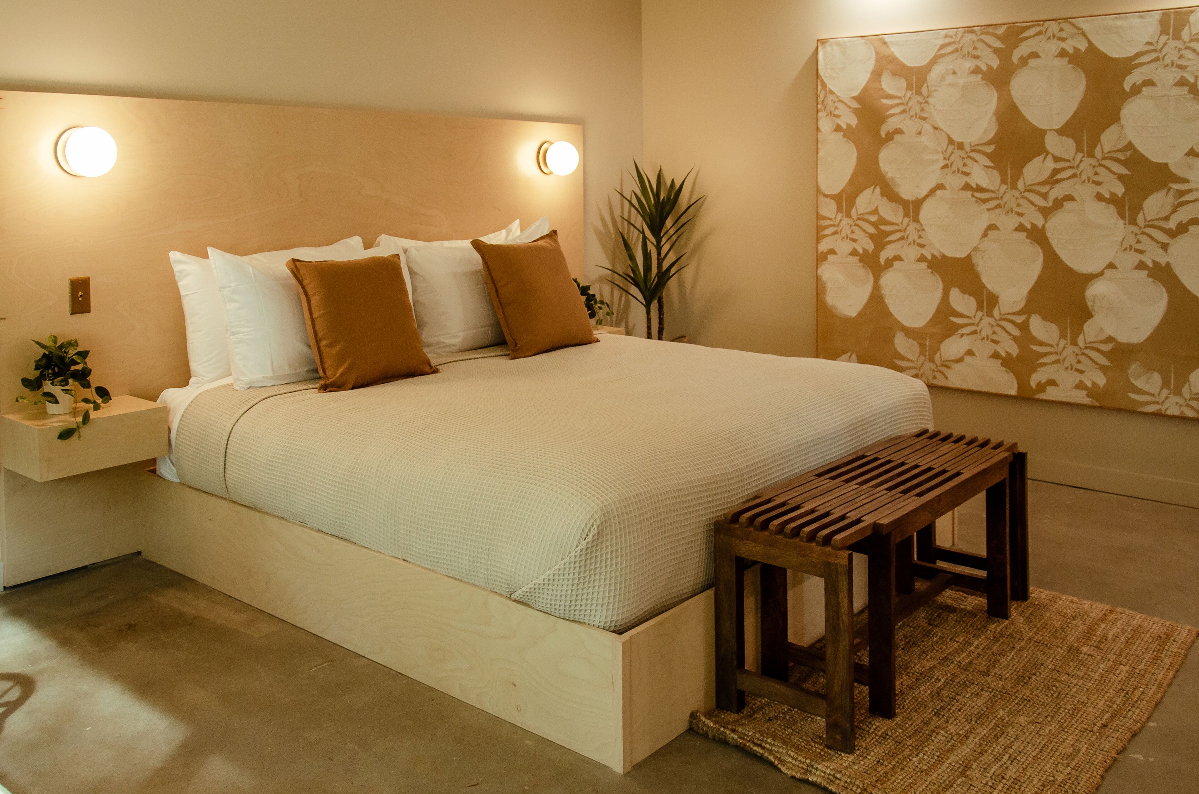 A neatly made bed with a headboard, a bedside table with a lamp, and a wooden bench.